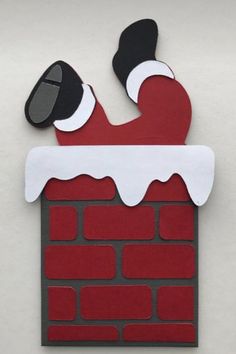 a paper cut out of santa claus stuck to a brick wall with his feet sticking out