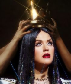 a woman with long black hair wearing a tiara and holding her head above her head