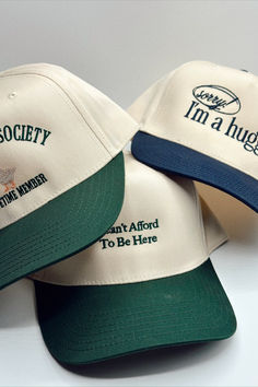 Three different cream and green or cream and blue trucker hats that read, "I can't afford to be here," "Silly goose society. Lifetime member," and "Sorry! I'm a hugger." Cheap Breathable Trucker Hat, Cheap Spring Trucker Hat With Curved Bill, Cheap Curved Bill Trucker Hat As Gift, Casual Khaki Trucker Hat Cheap, Cheap Fun Trucker Hat With Curved Bill, Cheap Adjustable Trucker Hat For Gift, Casual Wide Brim Trucker Hat, Affordable Urban Trucker Hat For Streetwear, Cheap Curved Brim Trucker Hat Gift