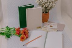 an open book sitting on top of a white table next to flowers and notebooks