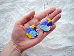 a hand holding two small beaded earrings