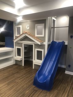 a blue slide in the middle of a room with white walls and wood flooring