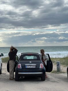 two cars parked on the side of the road with people standing next to them looking out at the ocean