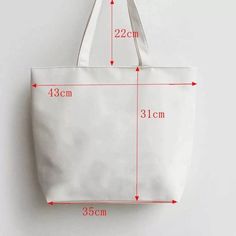 a white canvas tote bag with measurements for the size and width, hanging on a wall