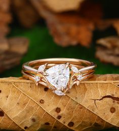 an engagement ring with three pear shaped diamonds on top of a leaf in the grass