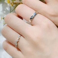 a woman's hand with two rings on her fingers and flowers in the background