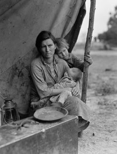 an old black and white photo of a woman holding a child on her lap while sitting in front of a tent