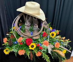 a cowboy hat and boots sit on top of a flower arrangement in front of a black curtain