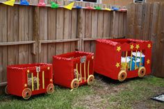 three red toy train cars sitting in the grass next to a fence with decorations on it