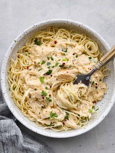 a white bowl filled with pasta covered in sauce and garnished with parsley