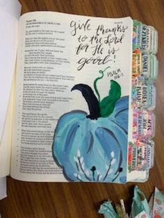 an open book on a wooden table with paper and scissors next to it that says give thanks to the lord for all who grace is good