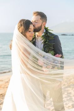 a bride and groom standing on the beach under a veil