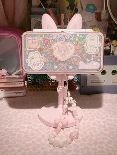 a pink hello kitty cell phone stand on top of a table next to other items