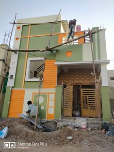 two men are working on the side of a house that has been built with orange and green paint