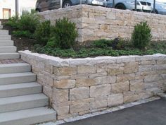 a stone wall with steps leading up to it and cars parked in the parking lot