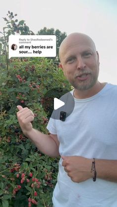 a man is standing in front of some flowers and pointing at the camera with his finger