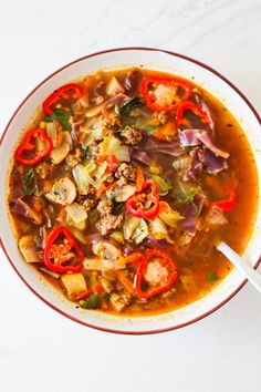 a bowl of soup with meat and vegetables in it on a white countertop next to a spoon