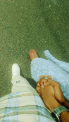 two people laying on the ground holding hands and touching each other's feet, with grass in the background