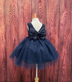 Our enchanting Knee Length flower girl dresses are sure to turn heads! This beautiful elegant sophisticated dress is handmade, the bodice consists of Navy Blue Sequin, the back of the dress consists of an open V-back with a zipper. The big bow is detachable. The skirt consists of 4 layers of Navy Blue  tulle with the top layer consisting with sowed in gold pearl beads. The fifth layer is made of lining with crinoline for fullness.  This dress is perfect for any occasion!  Dress Is Pictured with Elegant Blue Princess Dress With Bow, Elegant Blue Tutu Dress For Wedding, Blue Princess Tutu Dress With Bow, Princess Style Blue Tutu Dress With Bow, Elegant Blue Tutu Dress For Baptism, Elegant Fitted Tutu Dress For Pageant, Elegant Princess Wedding Dress With Bow Tie Back, Elegant Wedding Princess Dress With Bow Tie Back, Blue Princess Dress With Bow For Dress-up