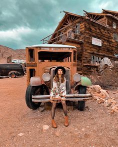 a woman sitting on the back of an old truck in front of a wooden building