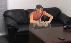 a man sitting on top of a black couch next to a wooden table with a remote control