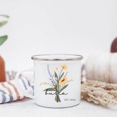 a white coffee mug with yellow flowers on it sitting next to a potted plant