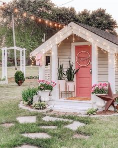 a small white house with pink front door and lights on the roof is decorated with potted plants