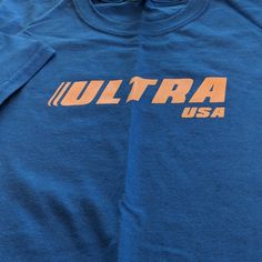 Ultra Brand Never Worn Blue Shirt With Text Print For Spring, Sporty Blue Shirt With Screen Print, Casual Blue Shirt With Text Print, Sporty Blue Shirt With Text Print, Casual Blue T-shirt With Text Print, Blue Cotton Pop Culture T-shirt, Blue Short Sleeve T-shirt With Logo, Functional Blue Moisture-wicking T-shirt, Applique Tee