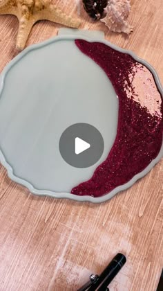 a wooden table topped with a bowl filled with red liquid next to a pen and starfish