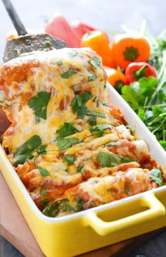 a yellow casserole dish filled with lasagna sauce and fresh herbs on the side