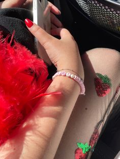 a woman's hand holding a cell phone with red feathers on it and strawberry stickers on her arm