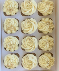 twelve cupcakes with white frosting and gold decorations in a box on a table