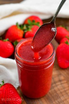 a spoon full of strawberry jam on top of a wooden cutting board with strawberries in the background