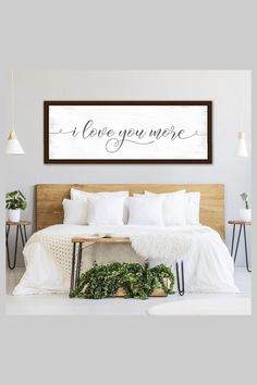 a bed with white sheets and pillows next to a wooden sign that says i love you more