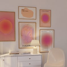 a white dresser sitting next to a wall with pictures on the wall and a lamp in front of it