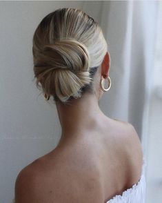 a woman with her hair in a low bun, wearing gold hoop earrings and a white dress