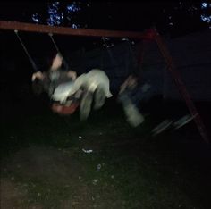 two people on swings in the dark at night, with one person falling off his back