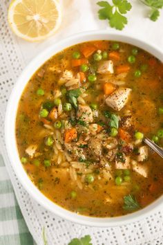 a bowl of chicken noodle soup with peas, carrots and parsley on the side