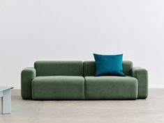 a green couch sitting in front of a white wall with a blue pillow on it