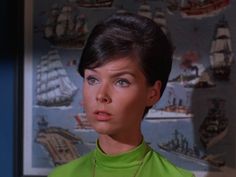 the woman is wearing a green shirt and looking off into the distance with ships on the wall behind her