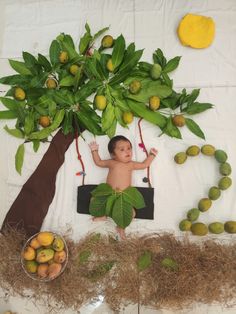 a baby is laying down in front of a tree with fruits and leaves on it