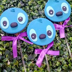 three blue cupcakes with googly eyes and purple ribbon on top of green plants