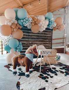 a horse is standing in front of balloons on the wall and chair, with other decorations hanging from the ceiling