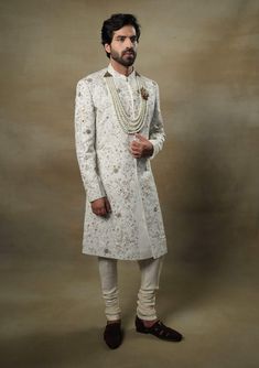 Editor's Note Featuring our work of art in our white all over hand-embroidered sherwani set. The foundation is crafted using machine embroidery adorned with tone on tone thread serving as the base texture, while the second tier showcases highlighting with 3D brass elements, dabka and zari threads. Fabric: Linen silk Color: Ivory, gold Components: Sherwani, kurta and churidar Occasion: Groom Fit: Regular Note: Product colour may slightly vary due to photographic lighting sources Care: Dry clean o Designer Off-white Bandhgala With Resham Embroidery, Designer Off White Festive Sets, Designer Off-white Traditional Wear With Chikankari Embroidery, Designer Off White Traditional Wear With Chikankari Embroidery, Formal White Raw Silk Traditional Wear, Designer White Raw Silk Sherwani, Designer Off White Traditional Wear With Resham Embroidery, Designer Traditional Wear With Resham Embroidery In Off White, Elegant Sherwani With Pearl Embroidery For Diwali