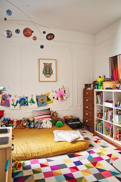 a child's bedroom with lots of toys on the floor and shelves full of books