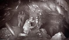 an old black and white photo of some people in a cave with one person holding something