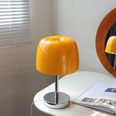 a yellow lamp sitting on top of a white table next to a mirror and magazine