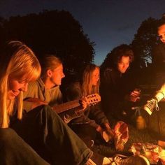 a group of young people sitting around a campfire playing guitars and singing to the music