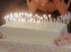 a woman blowing out candles on a white cake with pink flowers and roses around it