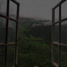 an open window looking out onto a lush green mountain valley in the foggy weather